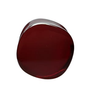 May include: A smooth, rounded, dark red glass object. The shape is irregular, with a polished, reflective surface. The object appears to be solid and opaque, with a slight sheen. The color is a deep, rich shade of red.