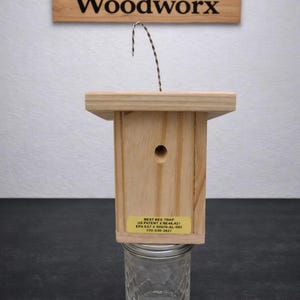 Puede incluir: Una trampa para abejas de madera clara con un orificio circular y un alambre met&aacute;lico para colgar. Un frasco de vidrio transparente est&aacute; sujeto en la parte inferior. Una etiqueta amarilla dice: BEST BEE TRAP US PATENT # RE48,421 EPA EST # 00079-AL-001 770-530-2621.