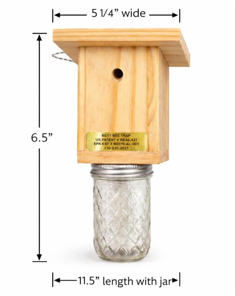 Puede incluir: Una trampa para abejas de madera con un frasco de vidrio transparente unido en la parte inferior. La trampa tiene una etiqueta dorada con el texto BEST BEE TRAP, US PATENT # RE46,421, EPA EST # 90079-AL-001, 770-530-2621. Las dimensiones son 13,3 cm de ancho, 16,5 cm de alto y 29,2 cm de largo con el frasco.