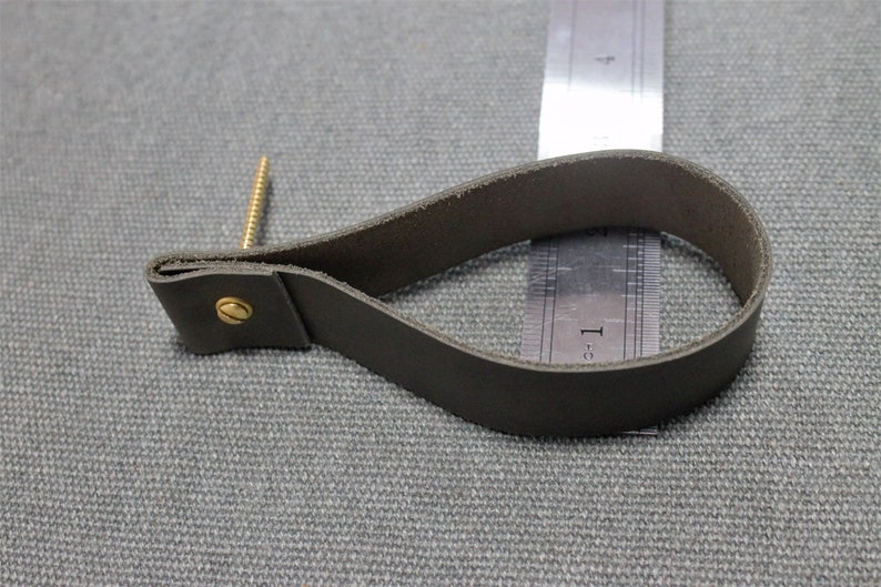 May include: A dark grey leather loop handle secured with a brass screw and fastener. A metal ruler is positioned behind the loop, showing the handle measures approximately 9 cm in length from the screw to the outer edge of the loop.