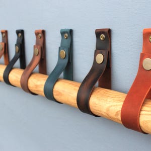 May include: A wooden rod with multiple leather hooks in various colours, including brown, blue, and red, mounted on a wall.