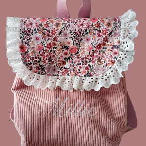 Peut inclure: Un sac à dos en velours côtelé rose poudré avec un rabat à motif floral bordé de dentelle blanche à œillets. Le prénom Millie est brodé en écriture blanche sur la poche avant. Le sac possède une poignée et des bretelles assorties.