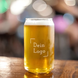 Könnte beinhalten: Ein klares Bierglas in Dosenform, gefüllt mit goldenem Bier und weißem Schaum. Das Glas trägt den Text "Dein Logo" in einem weißen Quadrat. Das Glas steht auf einer Holzoberfläche.