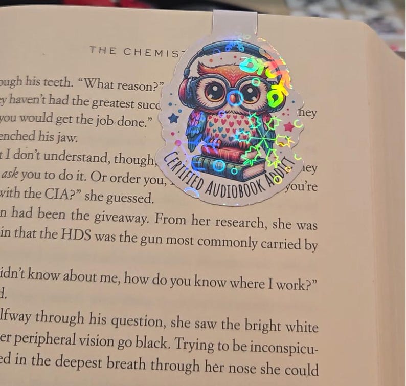 May include: A holographic bookmark featuring a cartoon owl wearing headphones and glasses, perched atop books. The owl has a heart-patterned chest and the text "CERTIFIED AUDIOBOOK ADDICT" is visible.