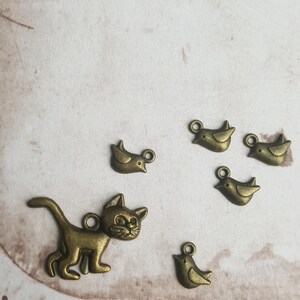 May include: A set of six metal charms featuring a cat and five birds. The charms are bronze in colour and have a vintage style.