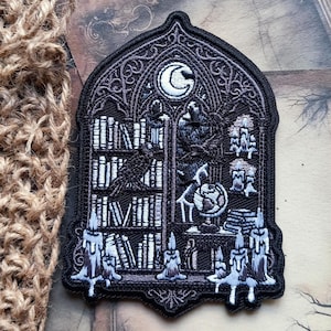 May include: An embroidered patch in the shape of a gothic arch window featuring a black and white scene of a library with bookshelves, a globe, and a raven. The design includes a crescent moon at the top and several lit candles at the base.