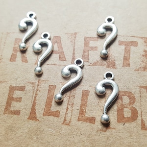 May include: Six silver question mark charms. The charms are in the shape of a question mark and have a loop at the top for attaching to a necklace or bracelet.