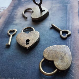 May include: A collection of bronze-finished, heart-shaped padlocks and keys. One padlock is open with a key inserted, others are closed. The keys have heart-shaped keyholes. The items are arranged on a textured, blue-toned surface, evoking a vintage aesthetic.