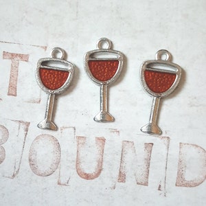 May include: Three silver charm pendants shaped like wine glasses with red enamel filling. The charms have a loop at the top for attaching to a necklace or bracelet.