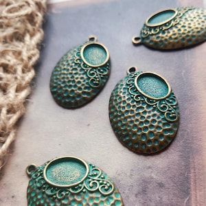 May include: Four oval-shaped metal pendants featuring a textured, honeycomb-like surface in a bronze and teal patina finish. Each pendant includes a small circular bezel setting at the top, accented with delicate scrollwork detailing and a loop.