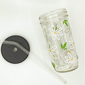 Peut inclure: Un pot en verre transparent avec un couvercle noir et un motif de marguerites blanches. Le pot a une paille et indique "LEAK-PROOF" sur le couvercle.