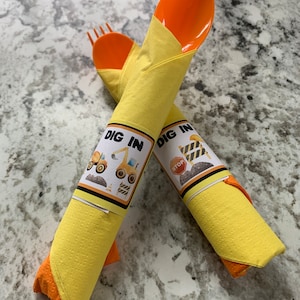 May include: Two yellow napkins with orange plastic forks wrapped inside. The napkins have a construction theme with the text "DIG IN" and a cartoon construction vehicle.