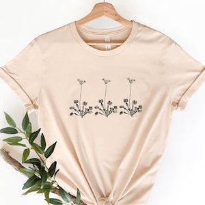 May include: A beige t-shirt with a simple black floral design printed on the front. The design features three stylized flowers with stems and leaves.