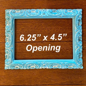May include: A light blue picture frame with an ornate design. The frame has a 6.25" x 4.5" opening.
