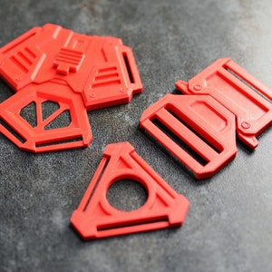 Può includere: Tre fibbie di plastica rossa di diverse forme e dimensioni. Le fibbie sono progettate per essere utilizzate con cinghie o cinture.