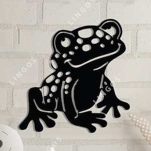 May include: Black silhouette of a frog with white spots, cut out of wood or metal. The frog is sitting on a white brick wall, with a wooden desk and other children's toys in the background.
