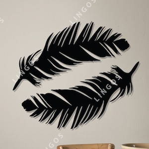 Puede incluir: Dos siluetas de plumas negras en forma de corazón sobre una pared de color beige claro. Las plumas están superpuestas. La imagen incluye el texto "DXF / CDR / Ai / SVG / PDF".