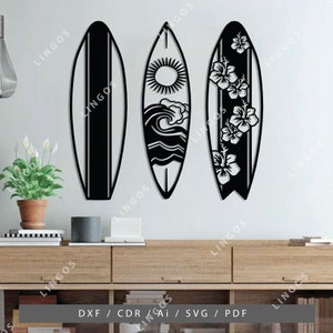 K&ouml;nnte beinhalten: Drei schwarze und wei&szlig;e Surfboard-Wanddekorationen. Die Surfboards sind mit einer Sonne, Wellen und Hibiskusbl&uuml;ten verziert.