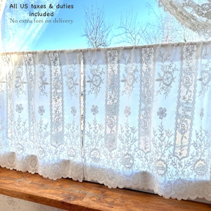 May include: White lace curtains with floral and leaf patterns hang in front of a window. The curtains are semi-sheer, allowing light to filter through. The bottom edge has a scalloped trim. The text "All US taxes & duties included" is visible.