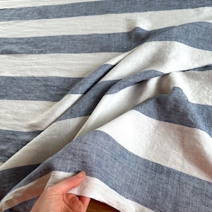 Könnte beinhalten: Nahaufnahme eines blau-weiß gestreiften Stoffes. Der Stoff ist gefaltet und zeigt seine Textur und sein Muster. Die Streifen sind breit und gleichmäßig angeordnet und erzeugen einen klassischen maritimen Look. Der Stoff scheint Leinen oder ein ähnliches Naturmaterial zu sein.