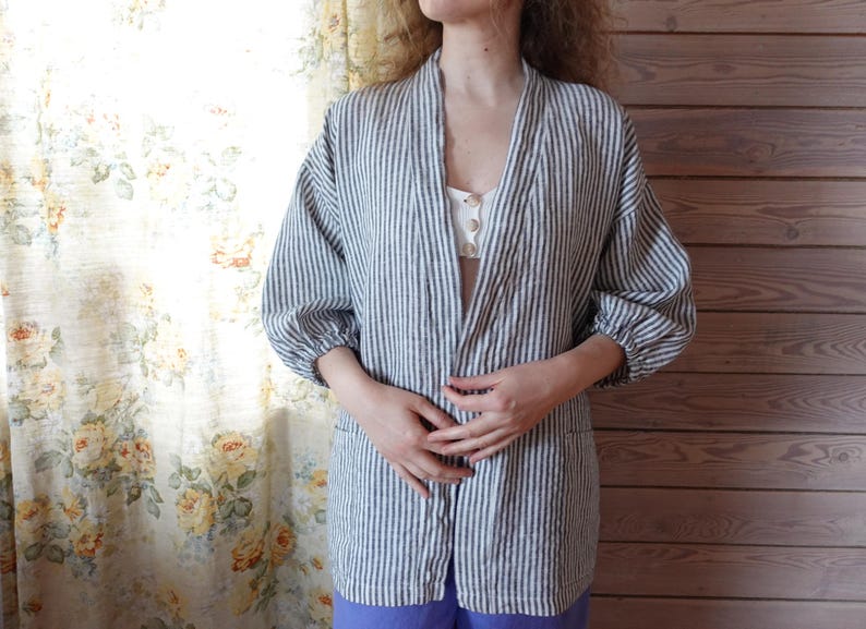 Puede incluir: Una chaqueta de lino a rayas blancas y azules de corte holgado y mangas largas. La chaqueta tiene cuello en V y cierre frontal.