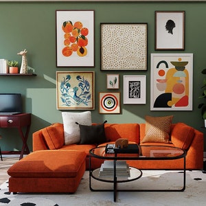 May include: A living room with an orange sectional sofa, a black coffee table, a white armchair, and a wall gallery featuring abstract art prints and a framed print of oranges.
