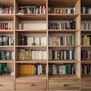 Può includere: Una libreria in legno con più ripiani pieni di libri. La libreria ha una finitura marrone chiaro ed è realizzata in legno massello.