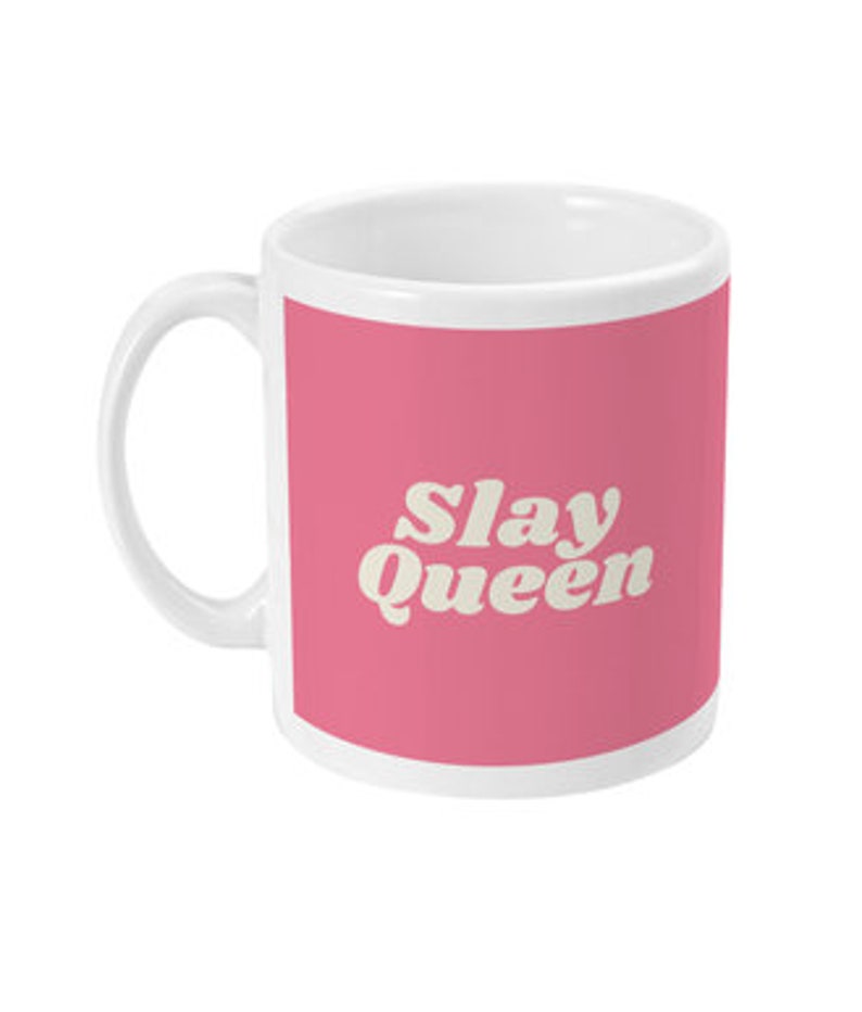 May include: White ceramic mug with a pink background and the text "Slay Queen" in a white retro font.
