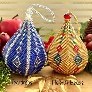 Puede incluir: Dos adornos de lágrima con cuentas. Uno es azul con detalles blancos y morados, el otro es dorado con detalles rojos, verdes y azules. Ambos tienen lazos de cuentas para colgar. El texto "Tear drops" y "HelenAtBeads" es visible.