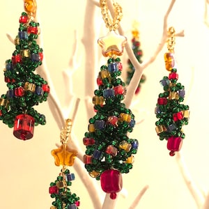 May include: A set of five beaded Christmas tree ornaments. The ornaments are made of green, red, blue, and yellow beads. The ornaments are hanging from a white branch.
