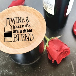 May include: A wooden wine bottle stopper with the text "Wine & friends are a great BLEND". The stopper is on top of a black wine glass. There is a red rose and a red rose petal in the background.