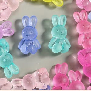 Op de afbeelding: Een verzameling doorschijnende konijnvormige bedels in verschillende pastelkleuren, waaronder blauw, roze, paars en groen. De bedels hebben een glanzende afwerking en zijn verspreid over een lichtgrijze ondergrond. Ideaal voor knutselen en het maken van sieraden.