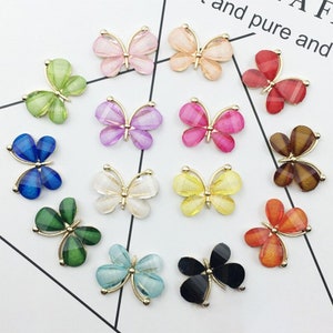 May include: Assortment of 12 colorful butterfly embellishments with gold accents. Each butterfly is made of clear plastic with a glittery finish. The butterflies are in various colors, including blue, green, red, pink, yellow, and white.