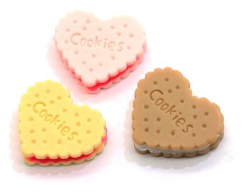 May include: Three heart-shaped cookies with pink, yellow, and brown frosting. Each cookie has the word "Cookies" written on it.