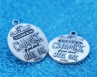 May include: Two silver-colored metal charms with the text "Don't expect to see a change if you don't make one." The charms are round with a small loop at the top for attaching to a necklace or bracelet.