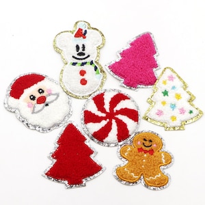 May include: A set of seven Christmas-themed felt patches with a silver glitter trim. The patches include a snowman, Santa Claus, a candy cane, a gingerbread man, and three Christmas trees.