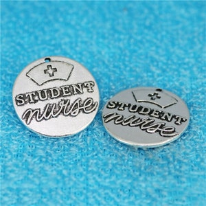 May include: Two silver-toned metal charms with the words "STUDENT NURSE" and a stylized image of a nurse's cap with a cross.