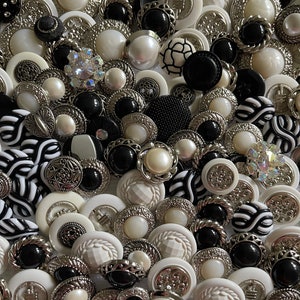 May include: A large collection of white and black buttons with silver accents. The buttons are various shapes and sizes, including round, square, and oval. Some buttons have a raised design, while others are smooth.