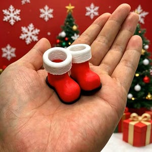 May include: A pair of miniature red boots with white cuffs, designed with a smooth finish and a rounded toe shape. These small decorative boots feature a solid red body and a textured white trim around the top opening, resembling classic holiday footwear.