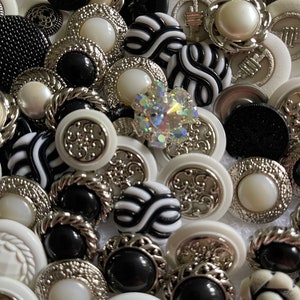 May include: A collection of black and white buttons with various designs and textures. Some buttons have a silver trim.