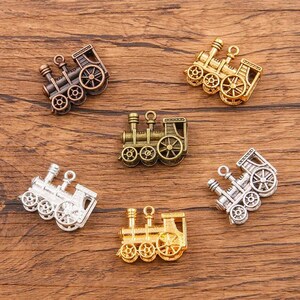 May include: Six miniature train engine charms in silver, gold, and bronze finishes. The charms are detailed with wheels, smokestacks, and other train features. They are perfect for adding a whimsical touch to jewelry or crafts.