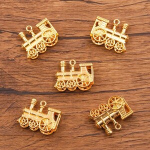 May include: Five gold-colored metal charms shaped like miniature train engines. Each charm has a loop at the top for attaching to a necklace or bracelet.
