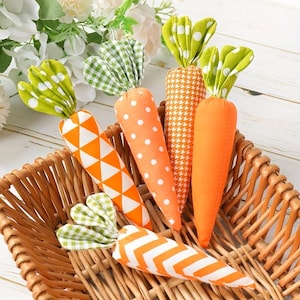 May include: A collection of decorative fabric carrots in a woven basket. The carrots are orange with various patterns, including polka dots, triangles, and stripes. The green tops have a leaf-like design. The basket is made of woven brown material.