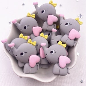 Könnte beinhalten: Eine Gruppe grauer Elefantenfiguren mit rosa Herzen und gelben Schleifen. Die Figuren sind aus Polymer Clay gefertigt und etwa 5 cm hoch.