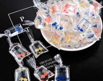 May include: A collection of small plastic bags filled with colorful plastic fish. The bags are tied with string and are arranged in a circle on a white plate. The plate is on a black surface.