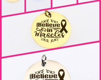 May include: Five round gold, silver, blue, and iridescent charms with the text "Believe in Miracles" and a pink ribbon. The charms have a loop at the top for attaching to a necklace or bracelet. The charms are displayed on a pink background with the text "Love Story" in white.