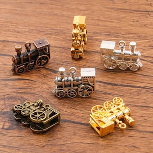 Puede incluir: Seis encantos de tren en miniatura en varios colores, incluyendo oro, plata y bronce. Los encantos están detallados con ruedas, chimeneas y otras características de tren. Son perfectos para agregar un toque caprichoso a las joyas o las manualidades.