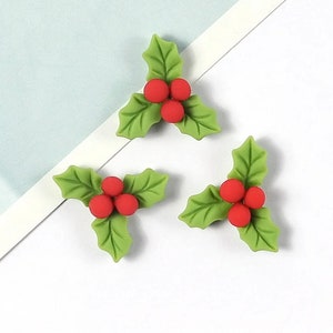 May include: Three green holly leaf ornaments with red berries. Each ornament has three berries.