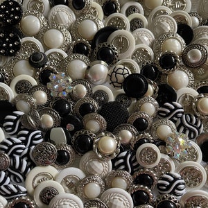 May include: A collection of black and white buttons with various designs and textures. The buttons are made of plastic, metal, and pearl. Some buttons have a silver finish.