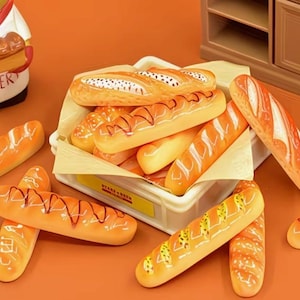 May include: A collection of miniature bread loaves, including baguettes and other types, arranged on a table. The bread has a golden-brown crust with decorative markings. A ceramic baker figurine and a small cabinet are in the background.
